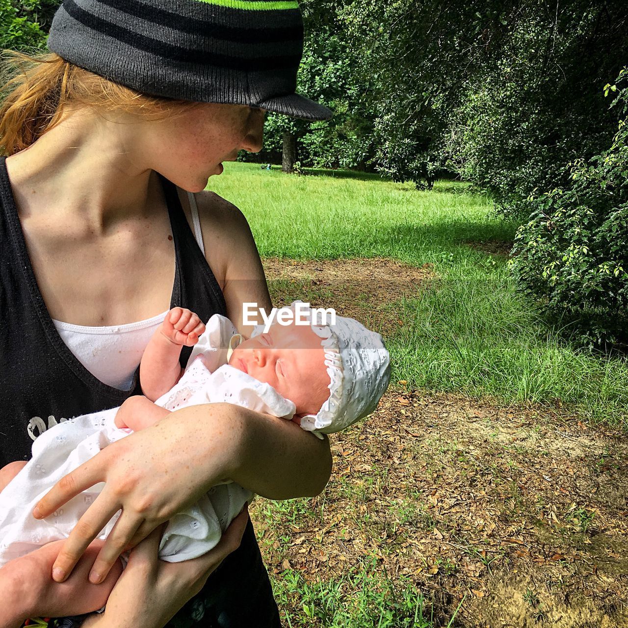 Girl holding newborn baby at park
