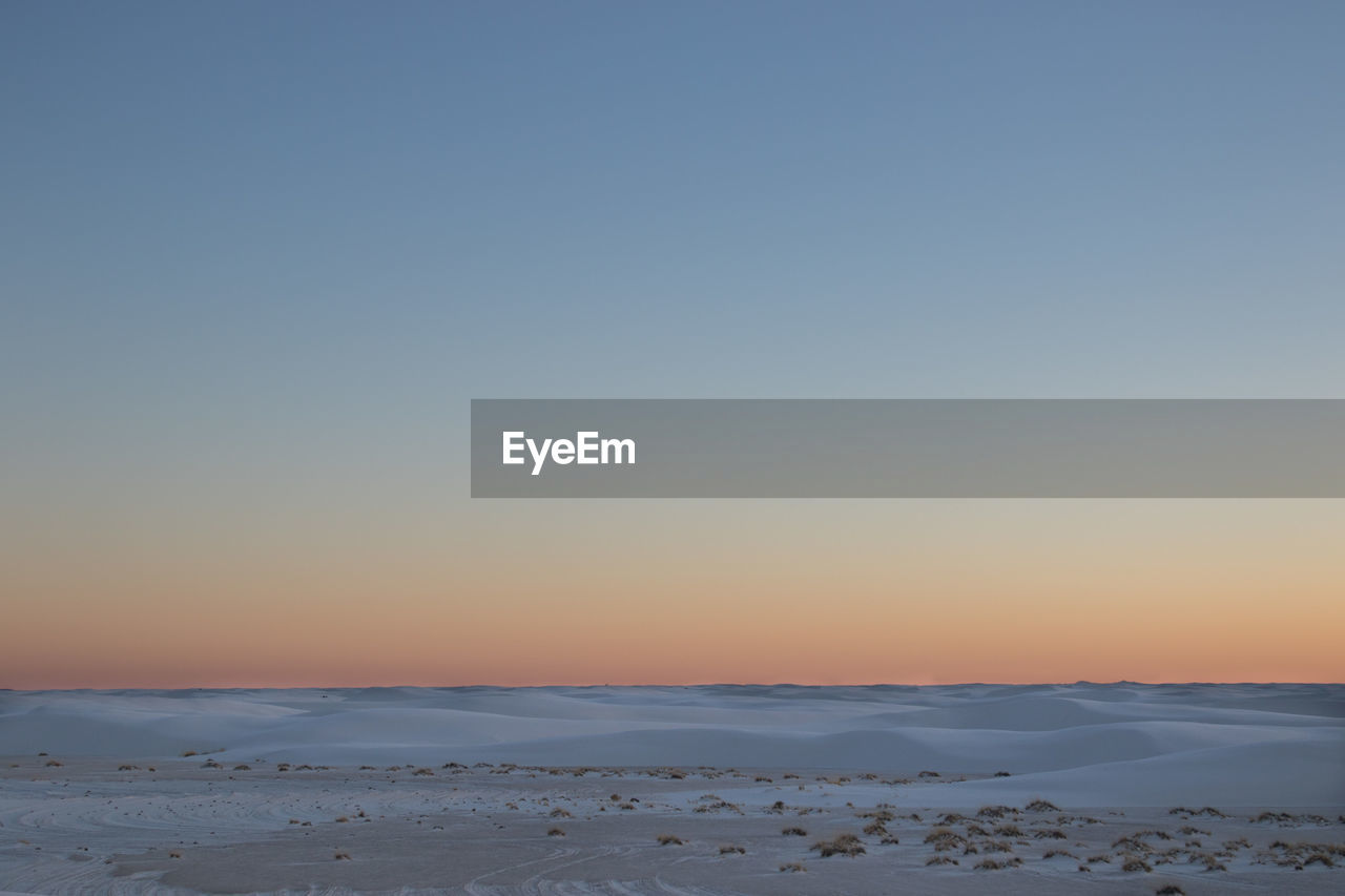 Scenic view of snow covered land against clear sky during sunset