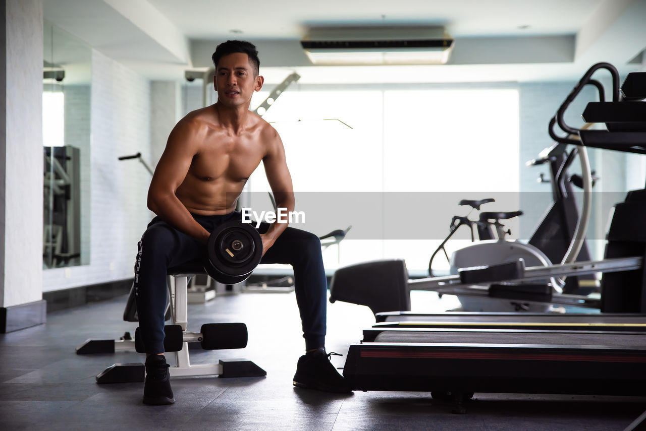 FULL LENGTH OF SHIRTLESS YOUNG MAN SITTING ON TABLE