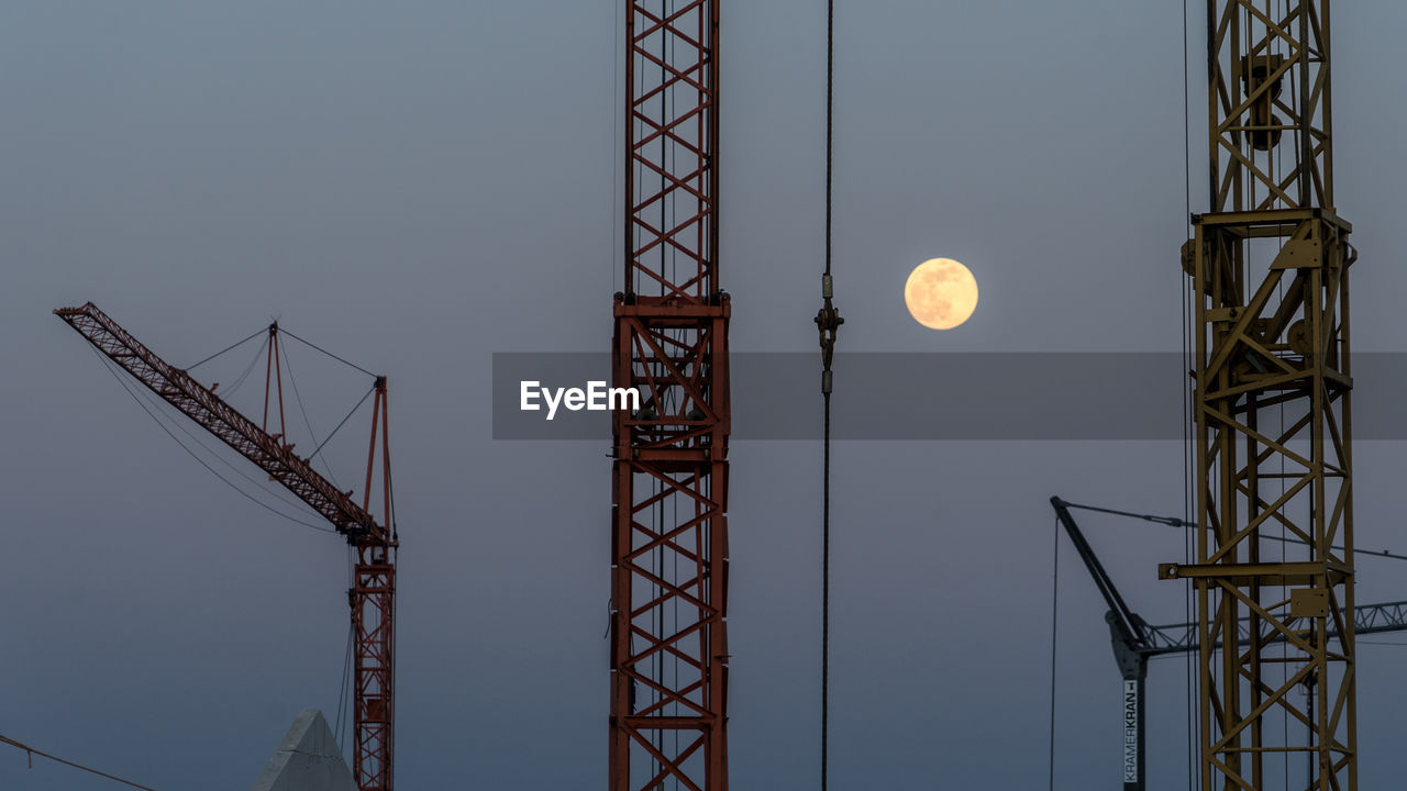 Low angle view of crane against sky at dusk with full moon