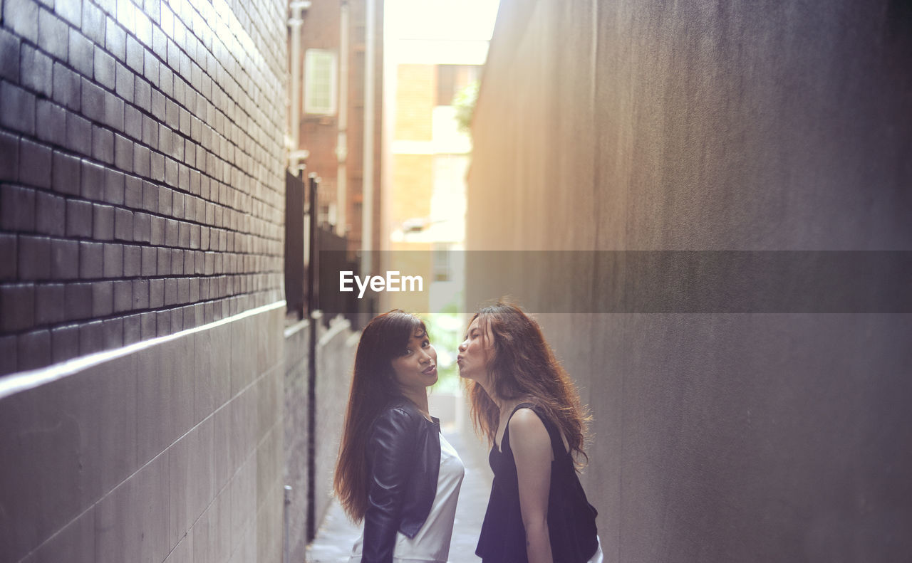 Portrait of woman standing with female friend puckering at alley