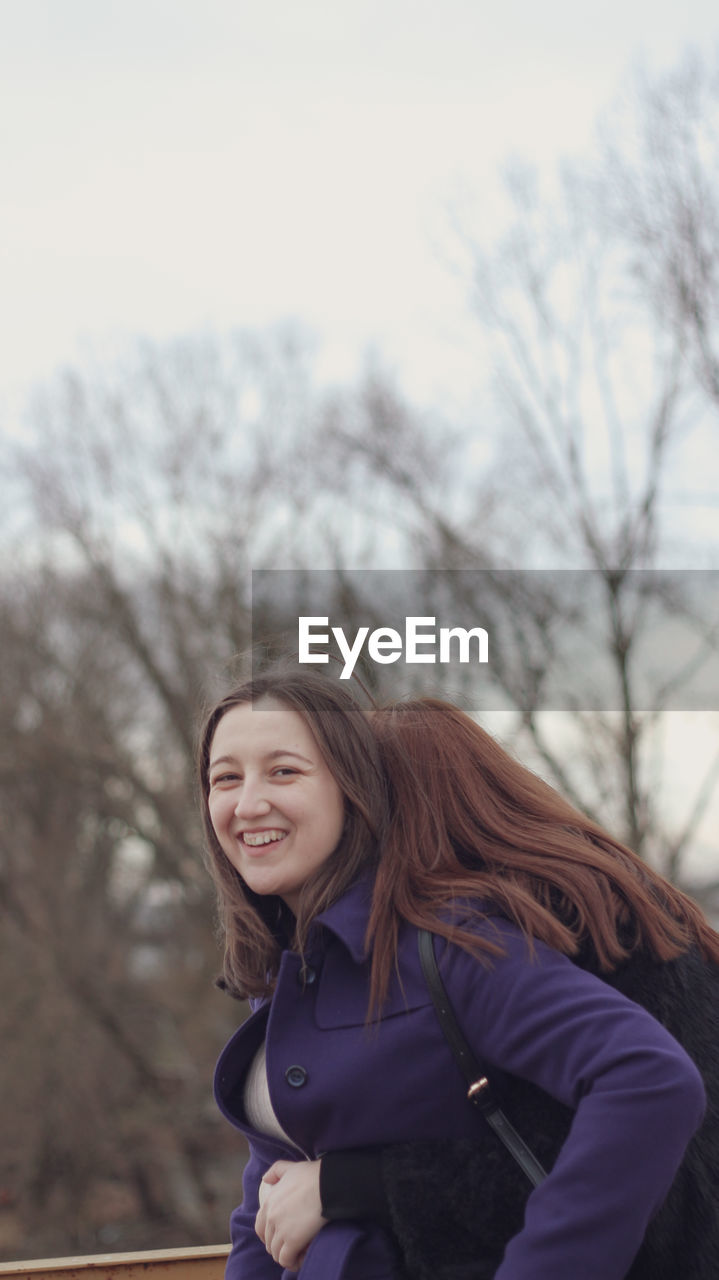 Portrait of a smiling young woman against bare trees