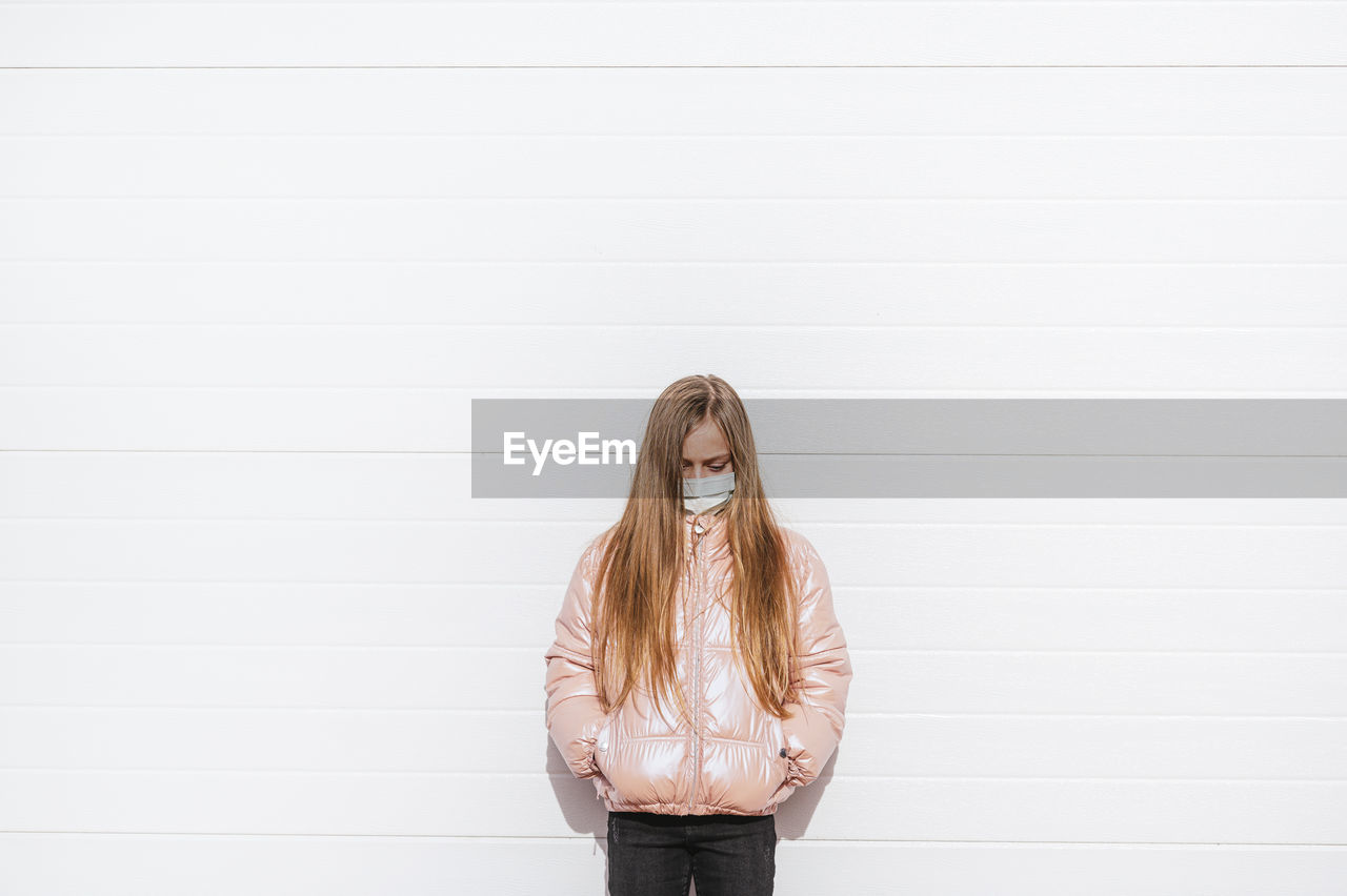 Girl wearing protective face mask standing against wall during covid-19