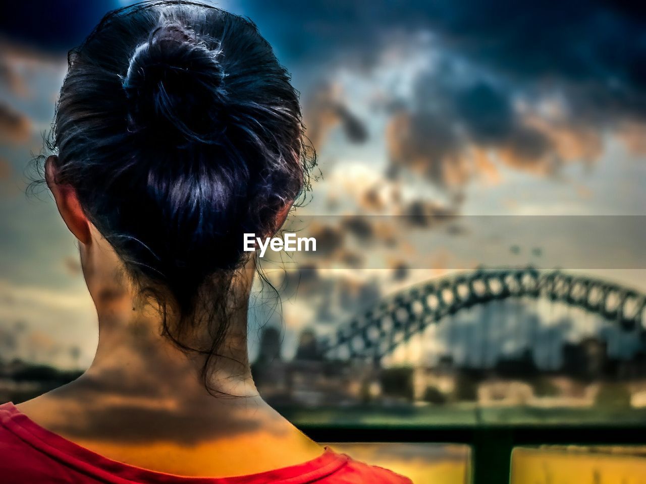 Rear view of young woman watching bridge against cloudy sky