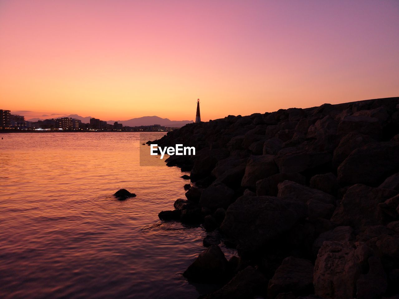 Silhouette rocks by sea against sky during sunset