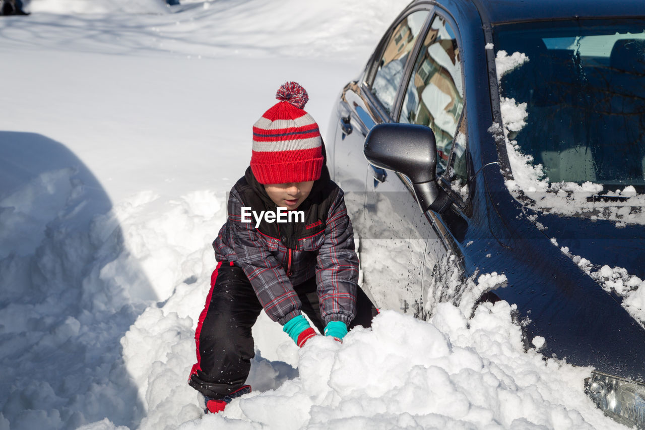 High angle view of boy playing with snow by car