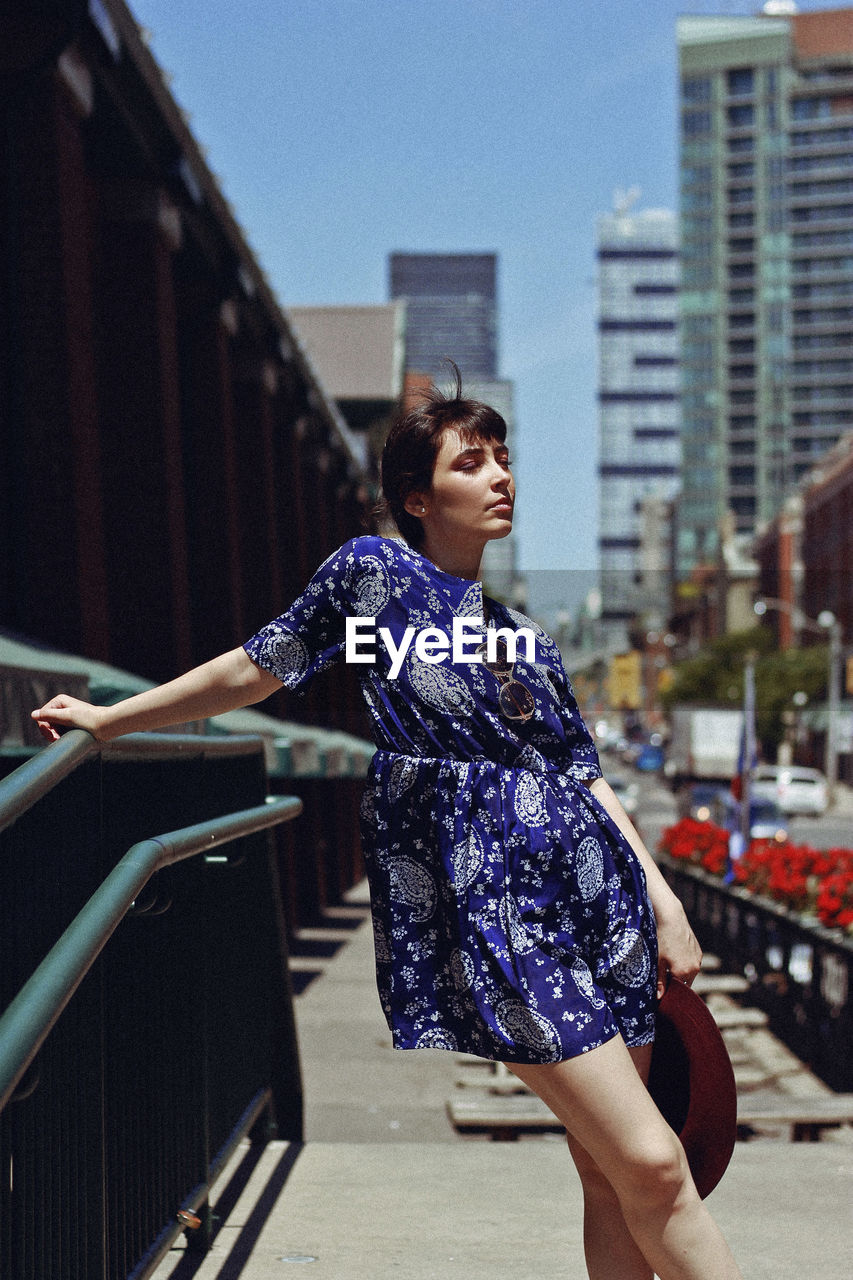 Woman leaning on railing on footpath in city