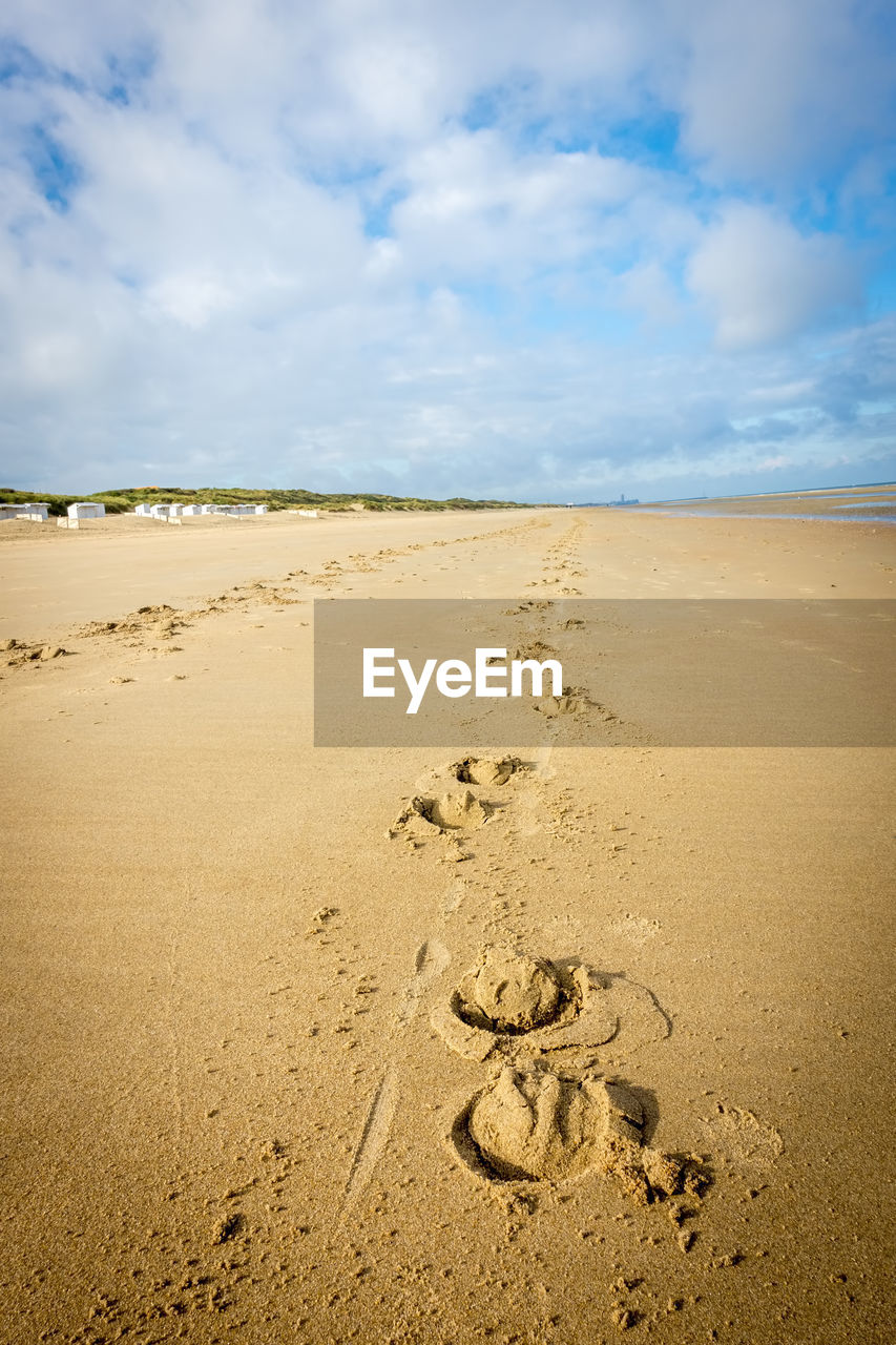 Footprints on sand at beach against sky