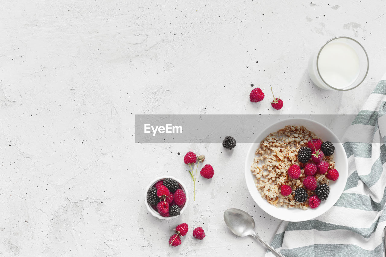 Morning healthy breakfast, white bowl full with granola, muesli, raspberry, blackberry on gray table