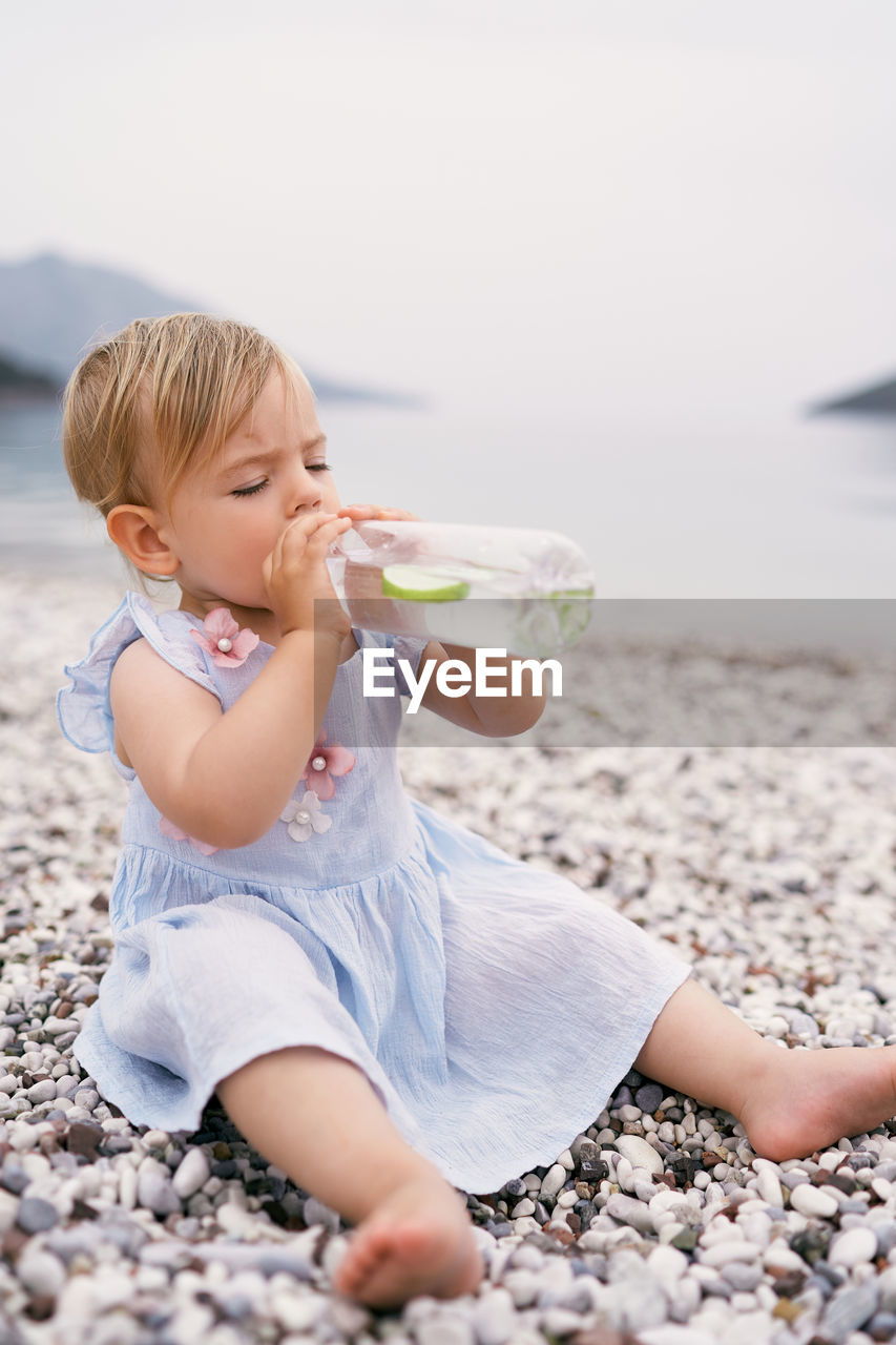 Full length of girl drinking lemonade sitting on beach