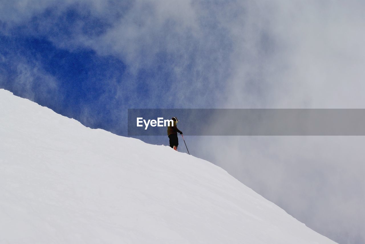 Person standing on snow covered slope against sky