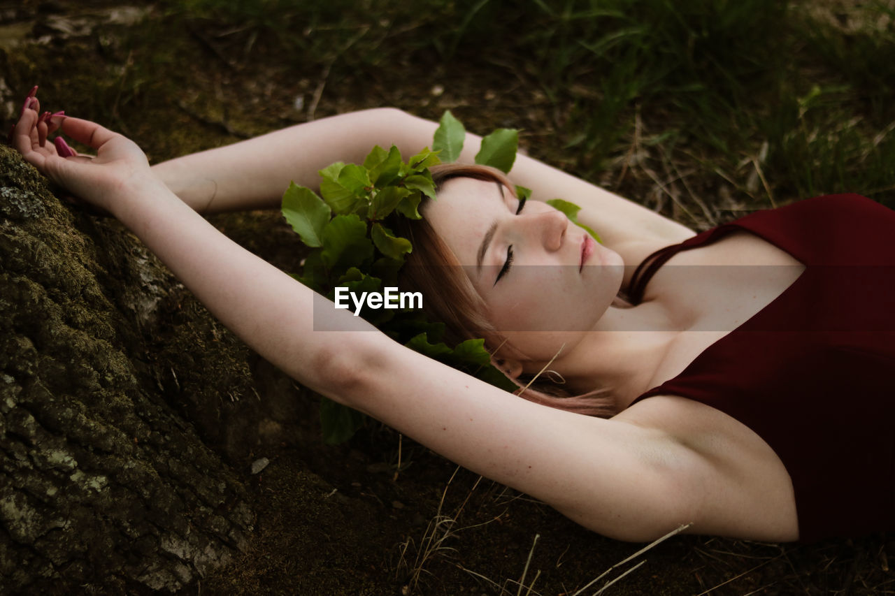 Midsection of woman young woman with closed eyes lying down on land wearing crown made of leaves 