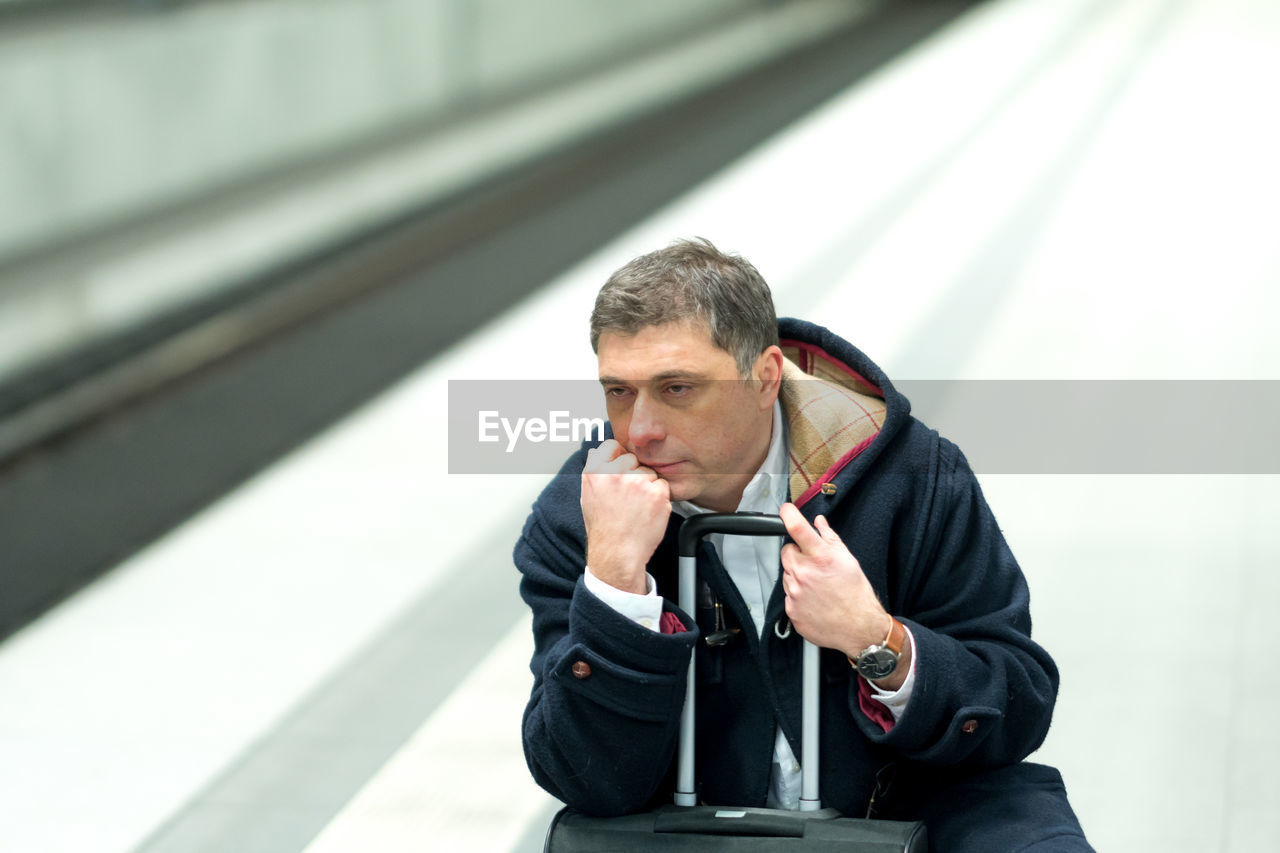 Man sitting on luggage at railroad station platform