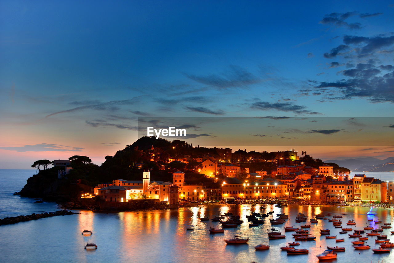 High angle view of boats moored on sea against illuminated buildings at sunset