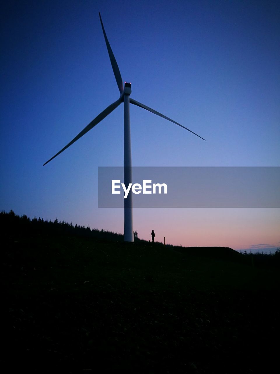 Silhouette of wind turbines on field against clear sky