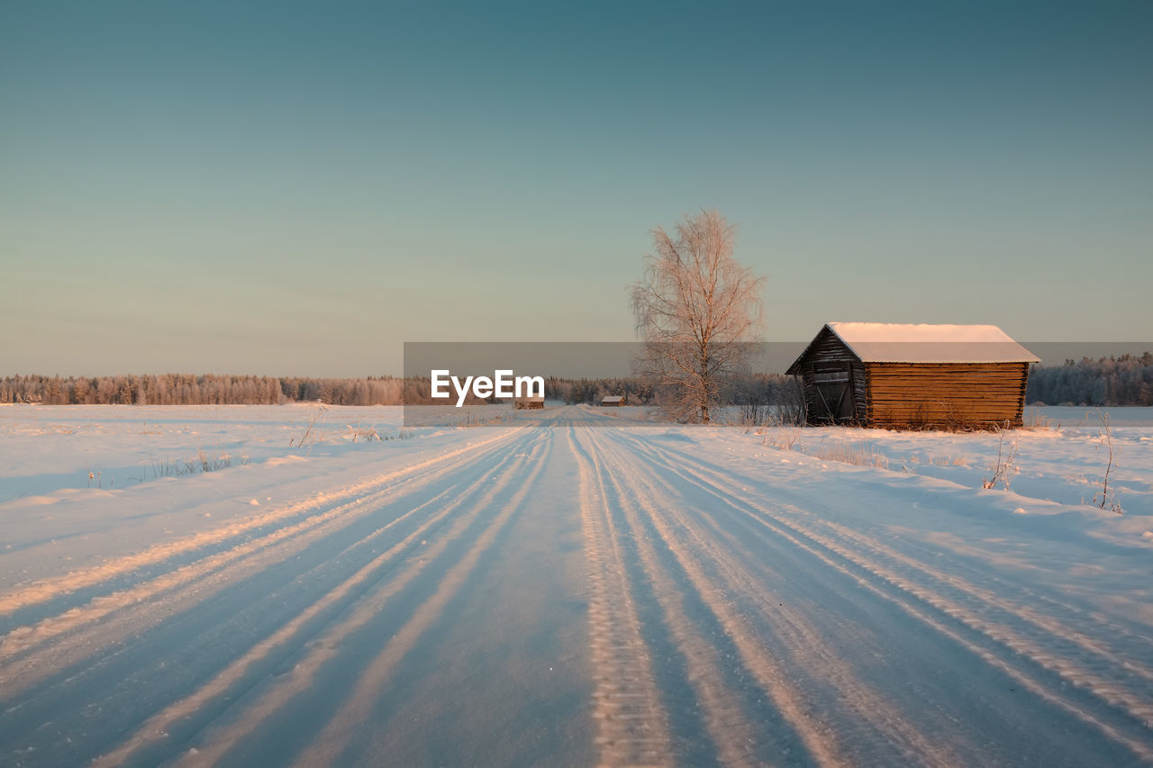 Frozen house on snowy landscape against clear sky during winter