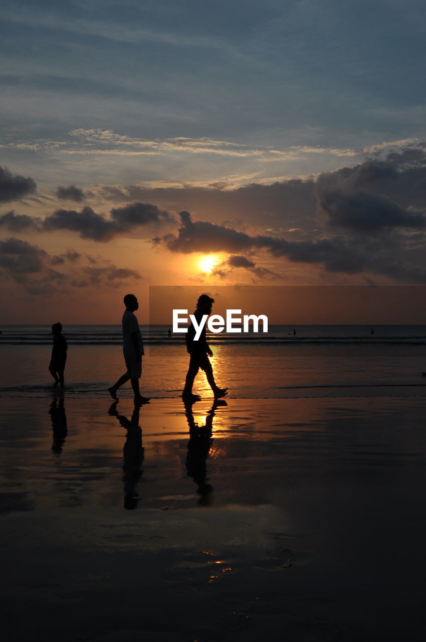 Silhouette men standing on beach against sky during sunset