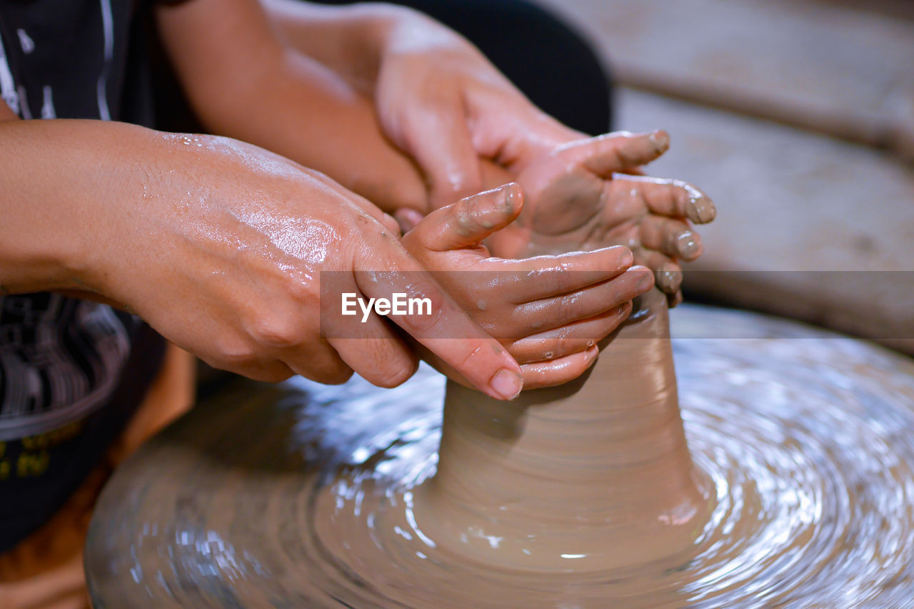 Midsection of people working on pottery wheel