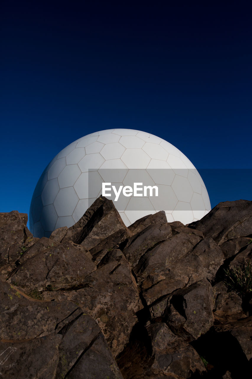 Low angle view of communication towers by rocks against clear blue sky