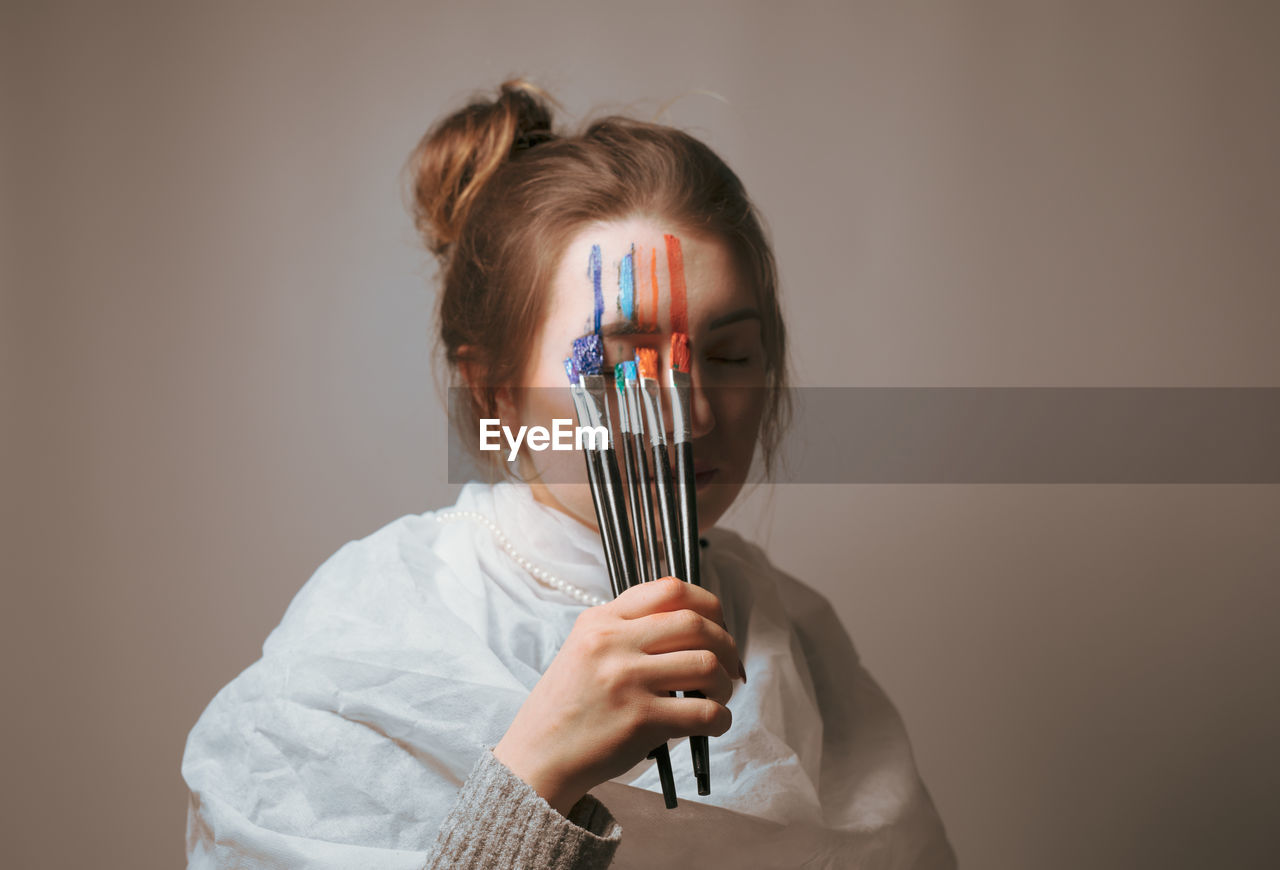 Young woman applying paint on face against wall