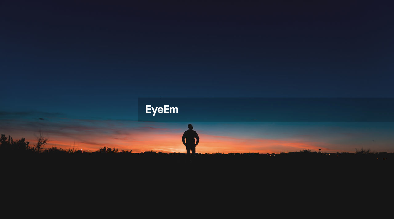 Silhouette man standing on field against sky during sunset