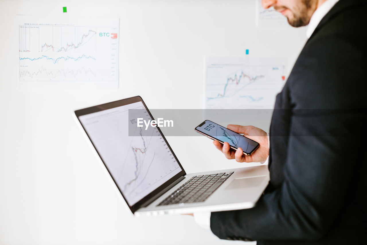 Midsection of businessman holding laptop and mobile phone at office