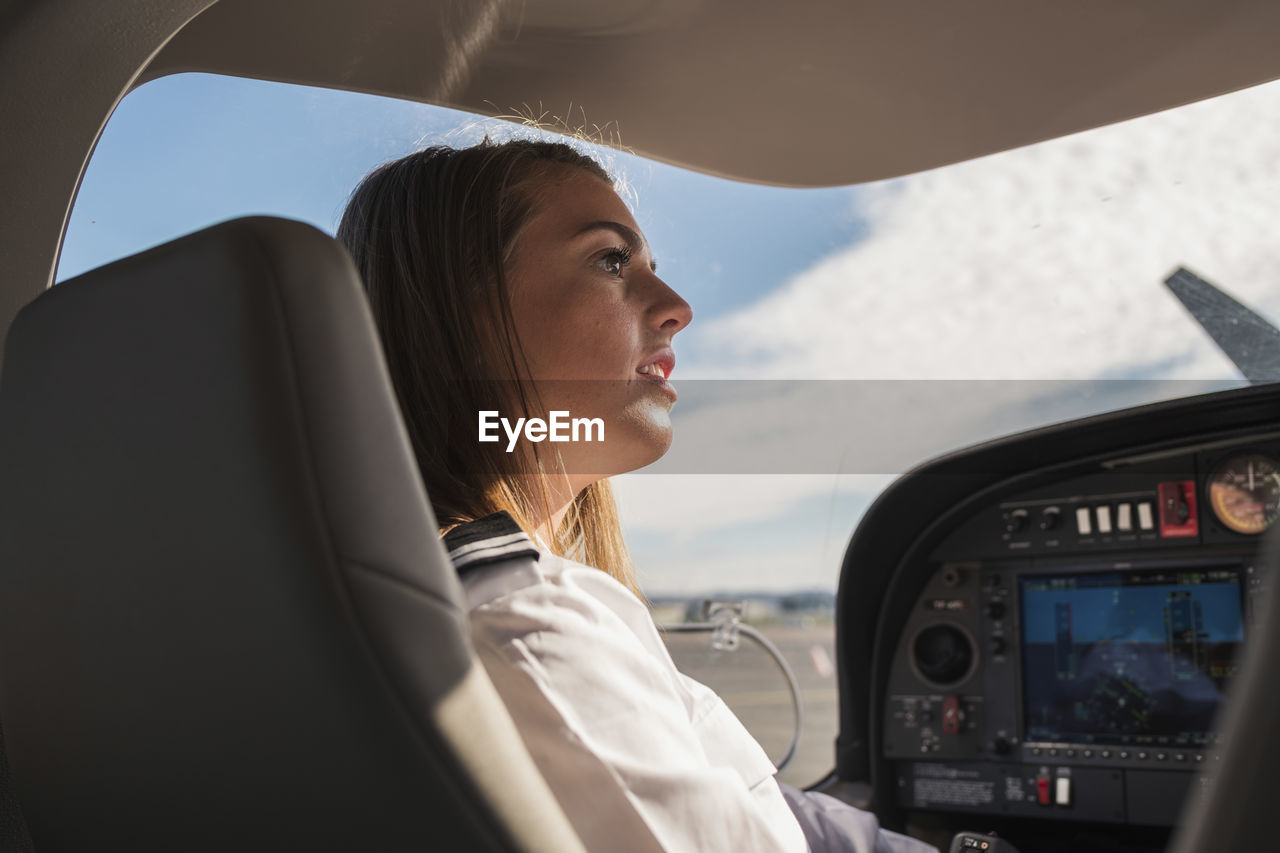 Side view of female pilot looking away while sitting in airplane at airport