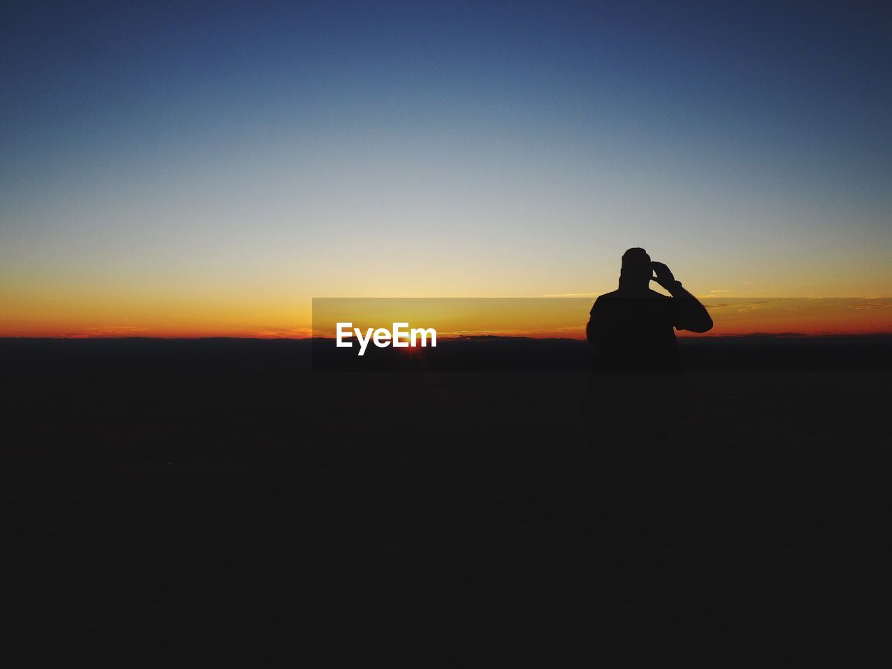 Silhouette man standing on field against sky during sunset