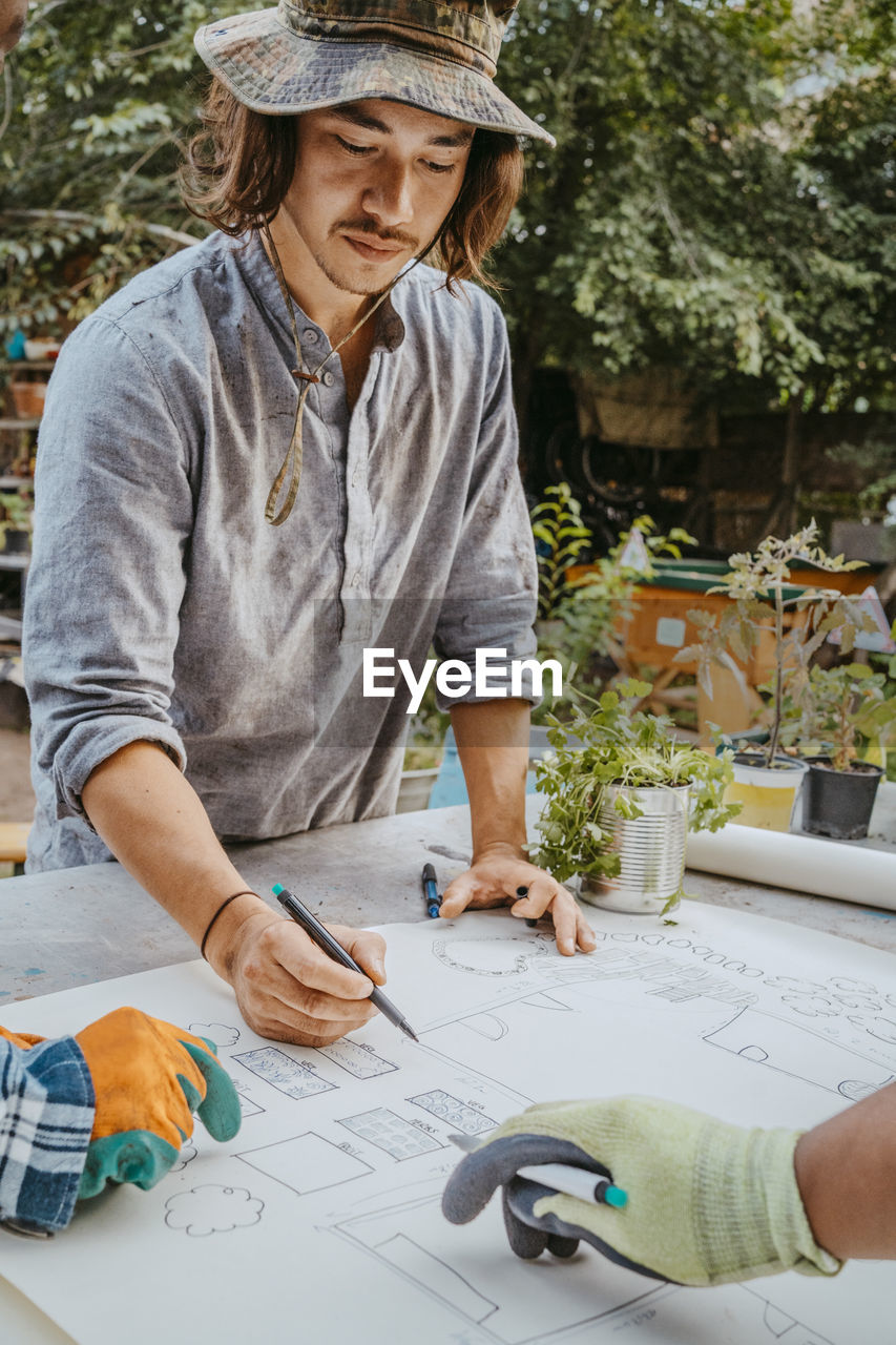 Young male volunteer drawing on paper at table in community garden