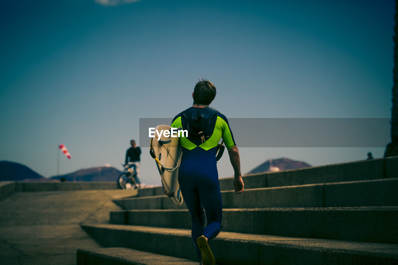 Rear view of man in wetsuit carrying surfboard