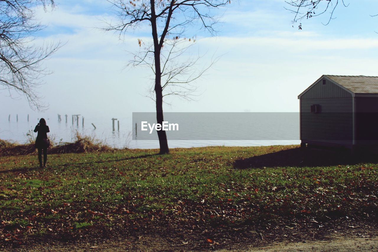 Rear view of woman standing on field against lake