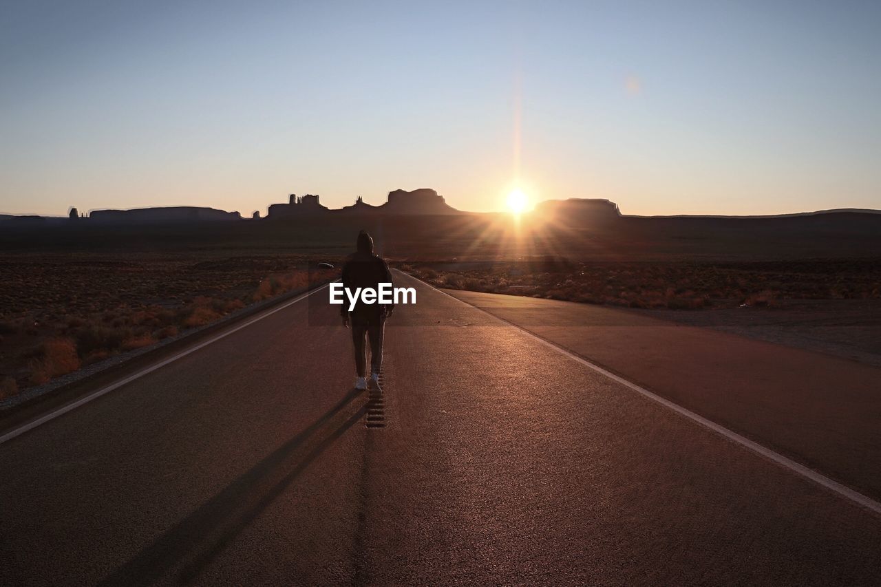 Rear view of man walking on road against sky during sunset