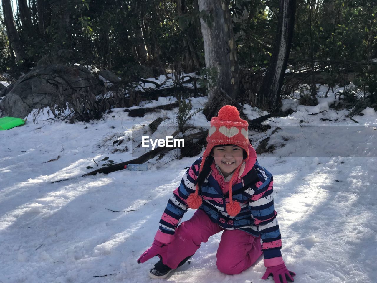 Portrait of girl wearing warm clothes while sitting on snow covered field during winter