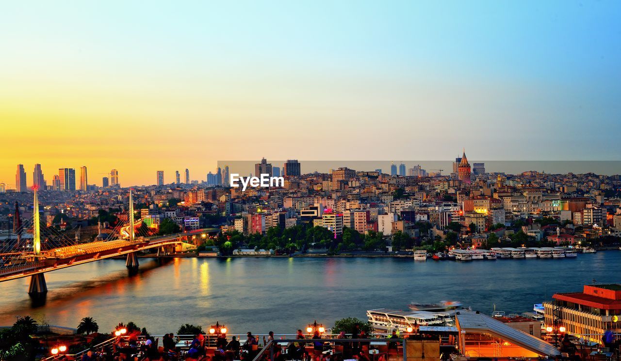 Panoramic view of illuminated buildings by river against sky during sunset