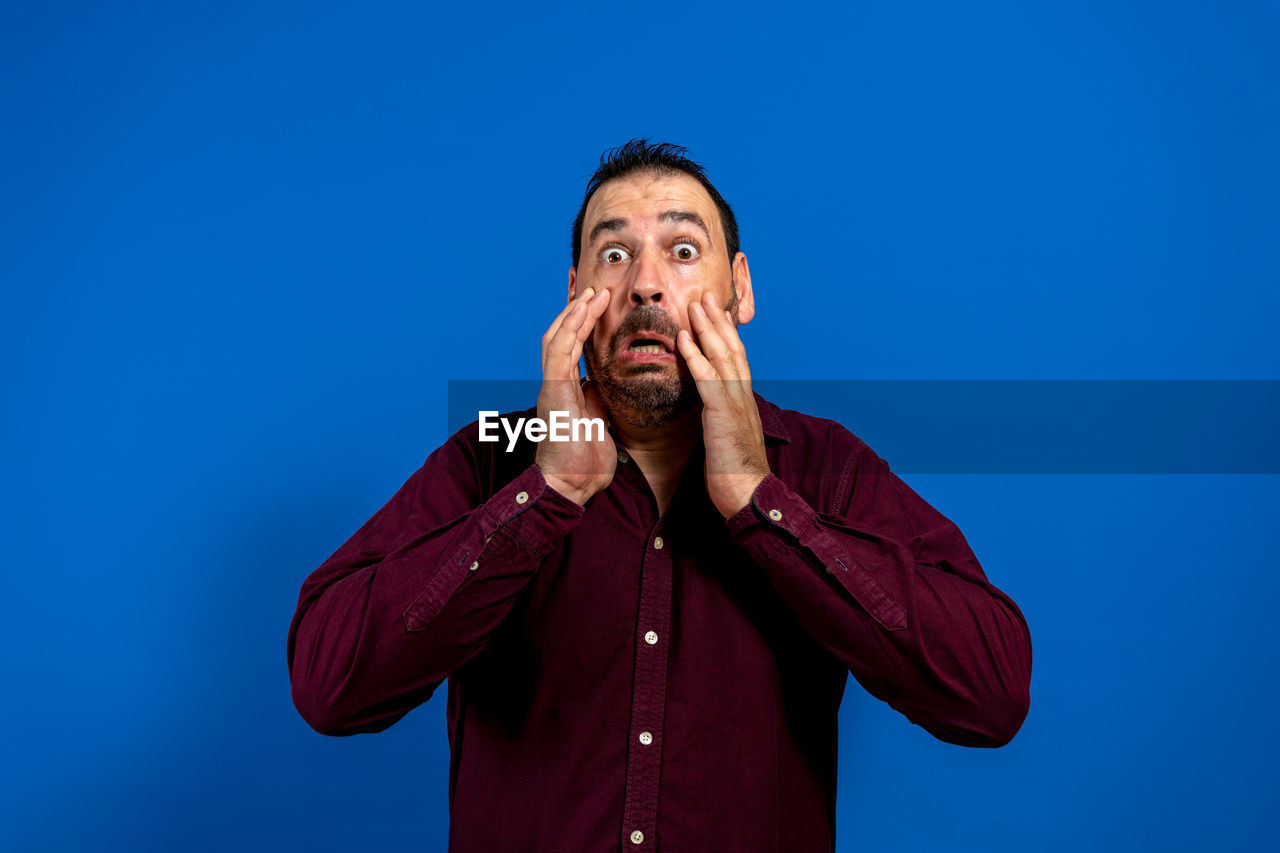 blue, one person, adult, men, singing, emotion, waist up, studio shot, blue background, colored background, copy space, portrait, front view, hand, looking, facial expression, person, standing, mature adult, negative emotion, sky, human face, indoors, casual clothing