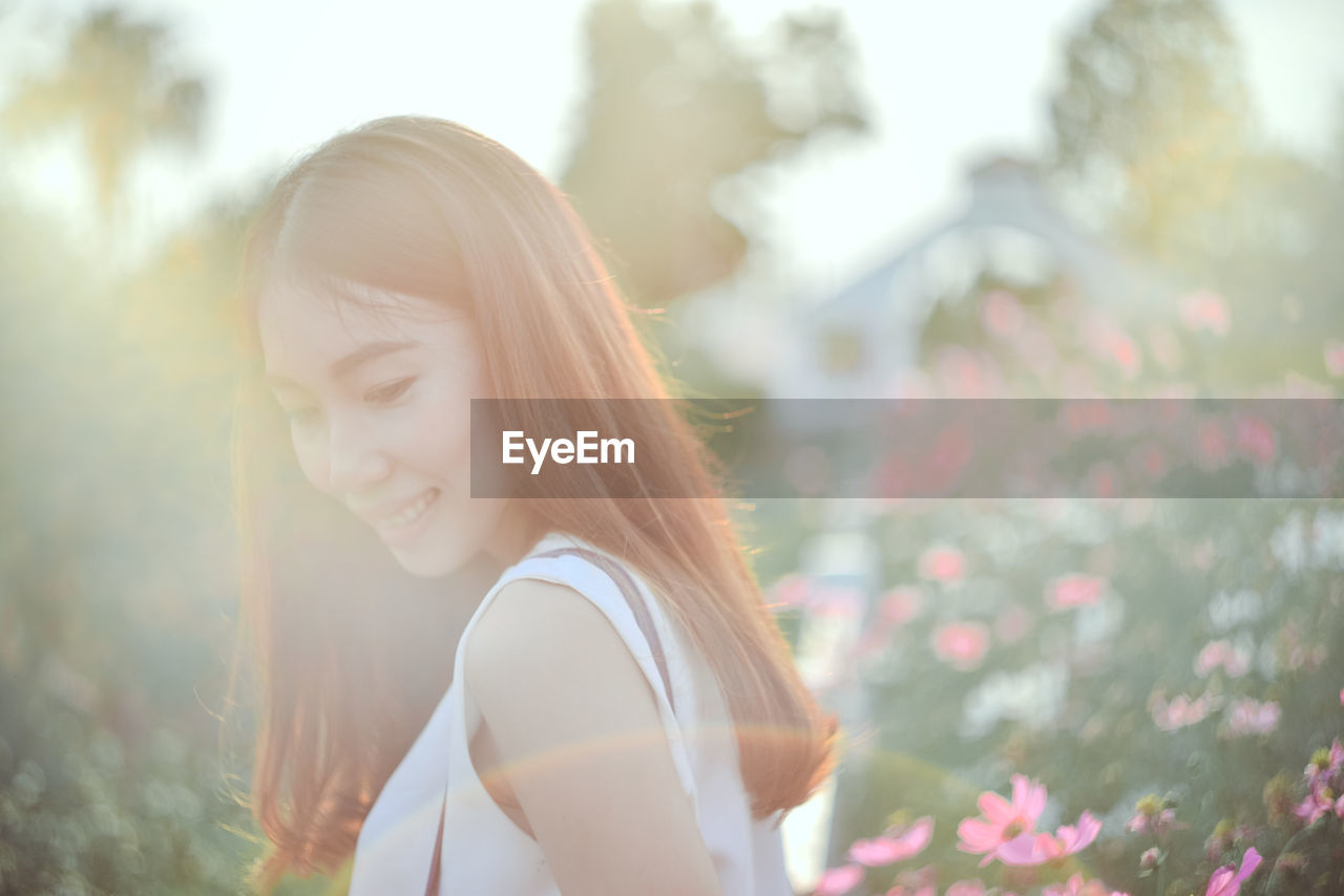 Side view of smiling young woman by flowers on field