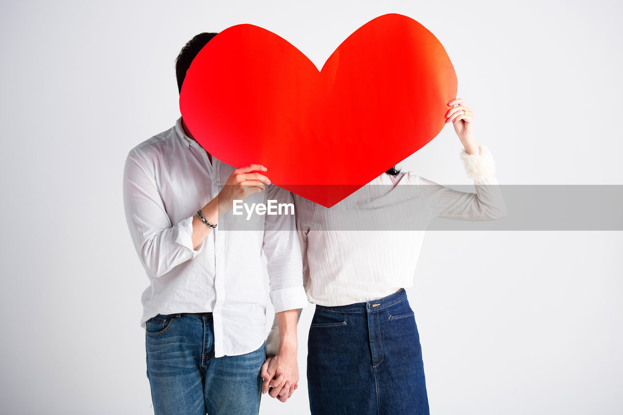 Midsection of couple with heart shape against white background