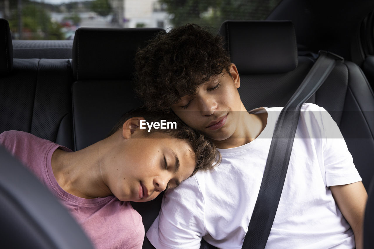 Tired brothers leaning on each other while resting in car