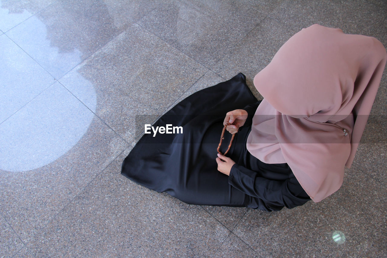 High angle view of woman in hijab holding counting rosary beads while praying at mosque