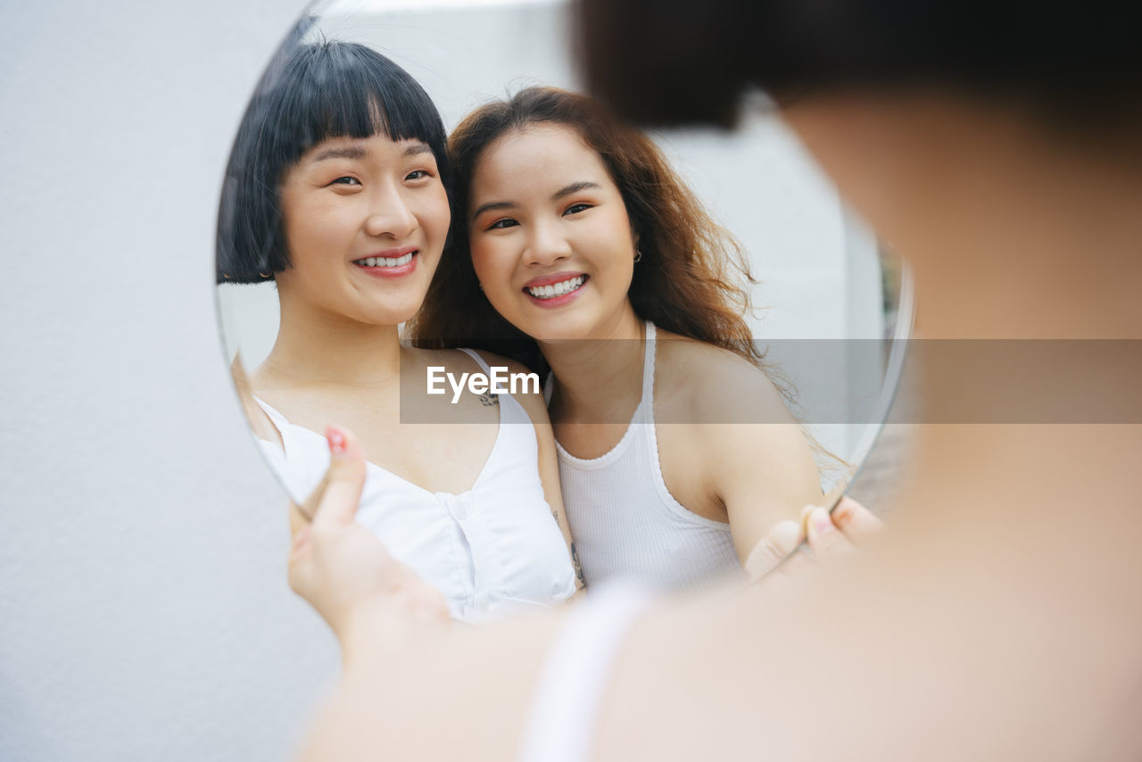 Reflection of lesbian sisters holding mirror outdoors