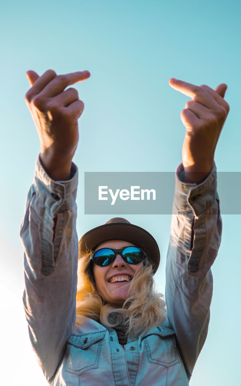 Woman in sunglasses showing obscene gesture against clear sky