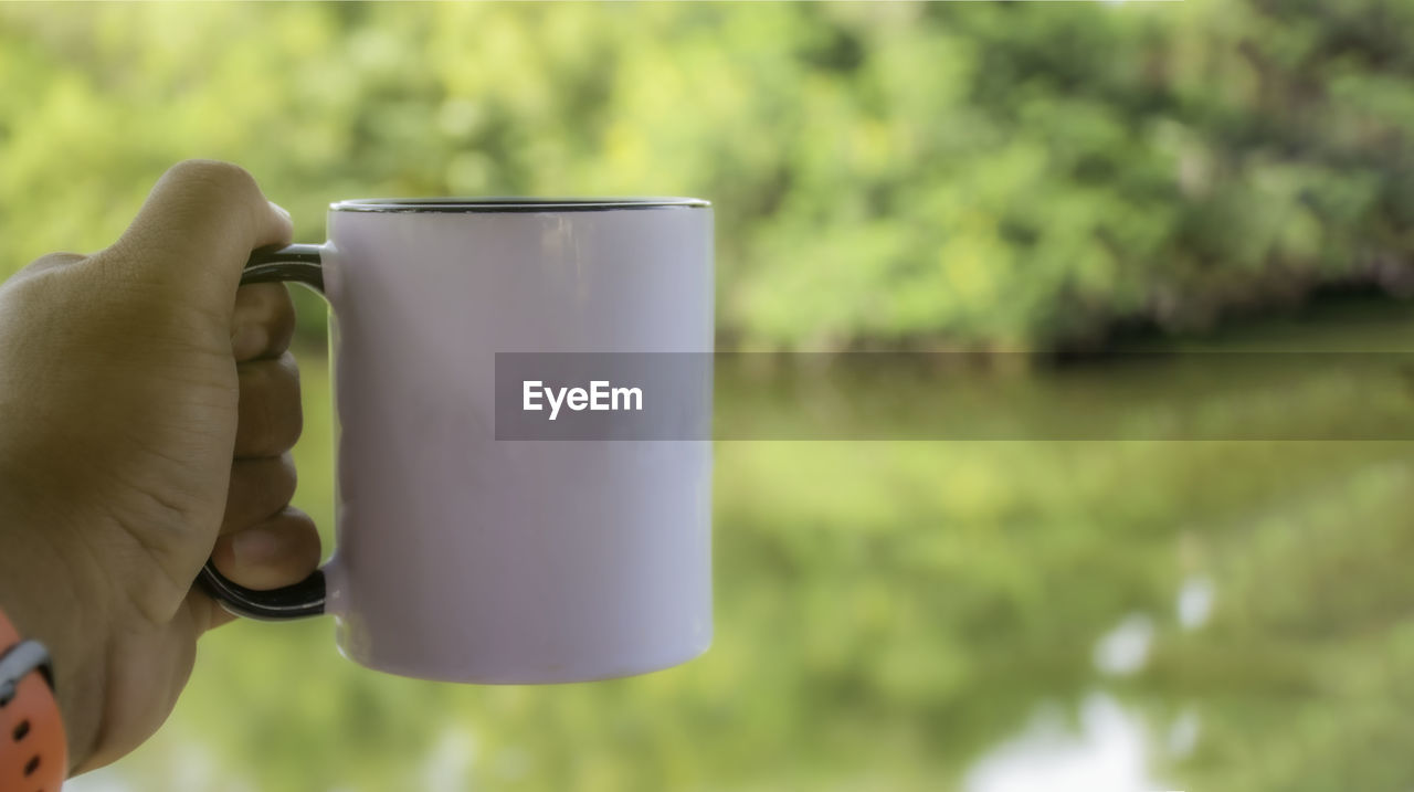 hand, mug, drink, holding, one person, coffee cup, refreshment, cup, focus on foreground, food and drink, nature, adult, day, water, green, close-up, plant, outdoors, lifestyles, tableware, coffee, leisure activity