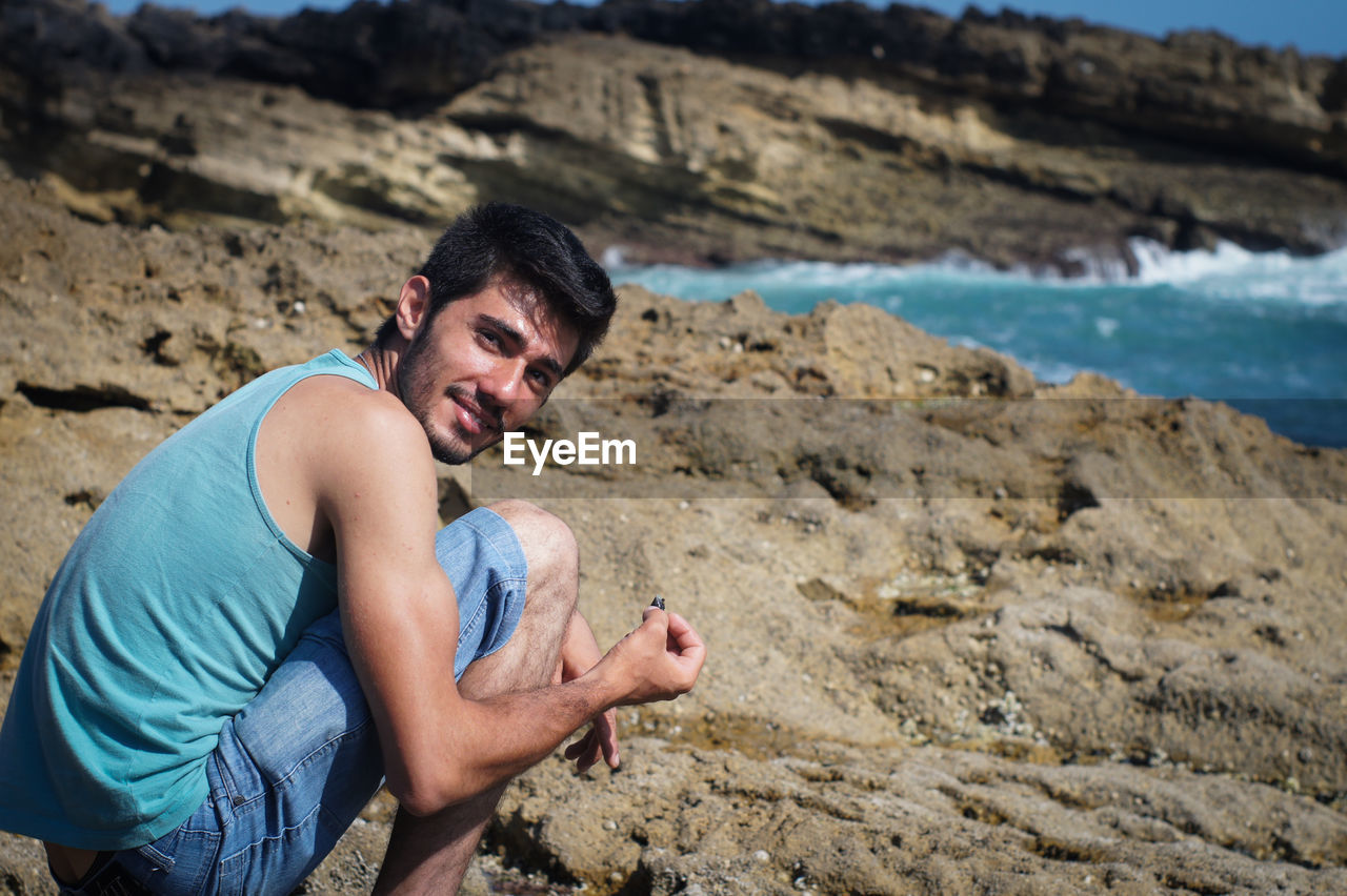 Portrait of smiling man crouching on shore at beach