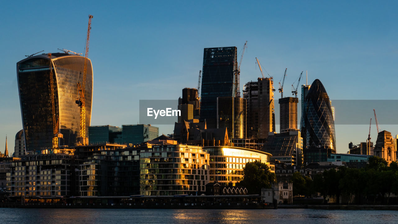 Skyscrapers by river against sky in city