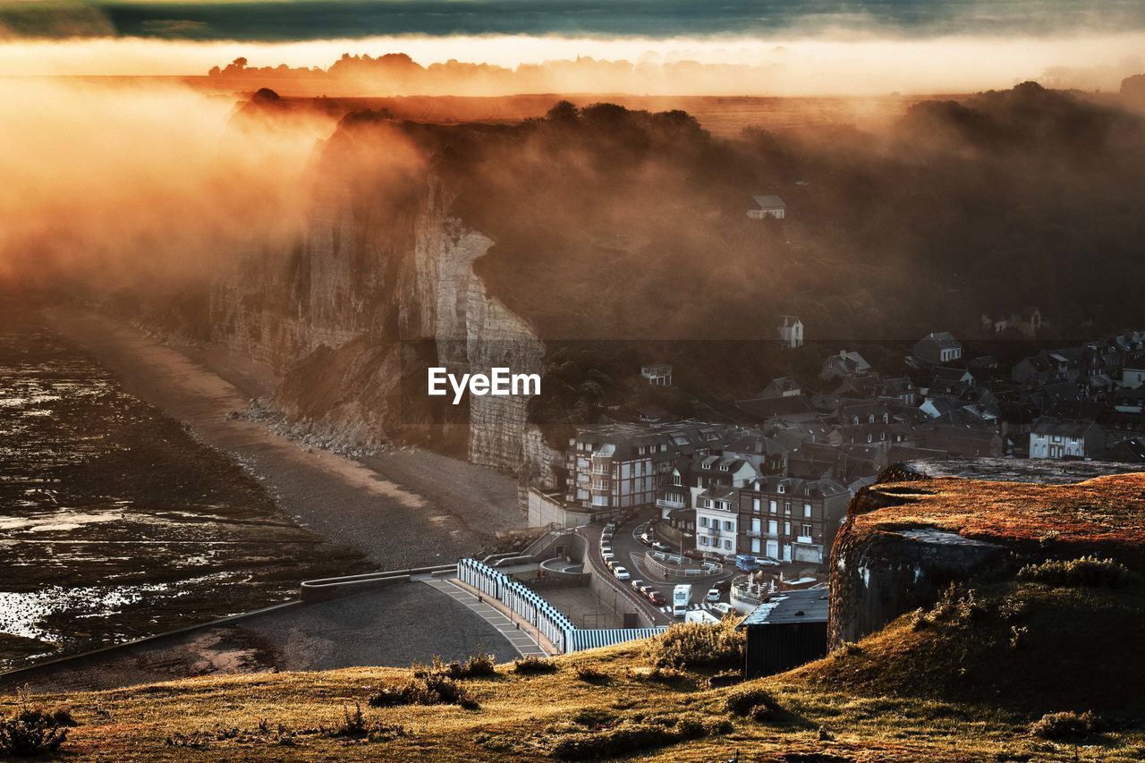 High angle view of buildings in town by mountain during foggy sunset 