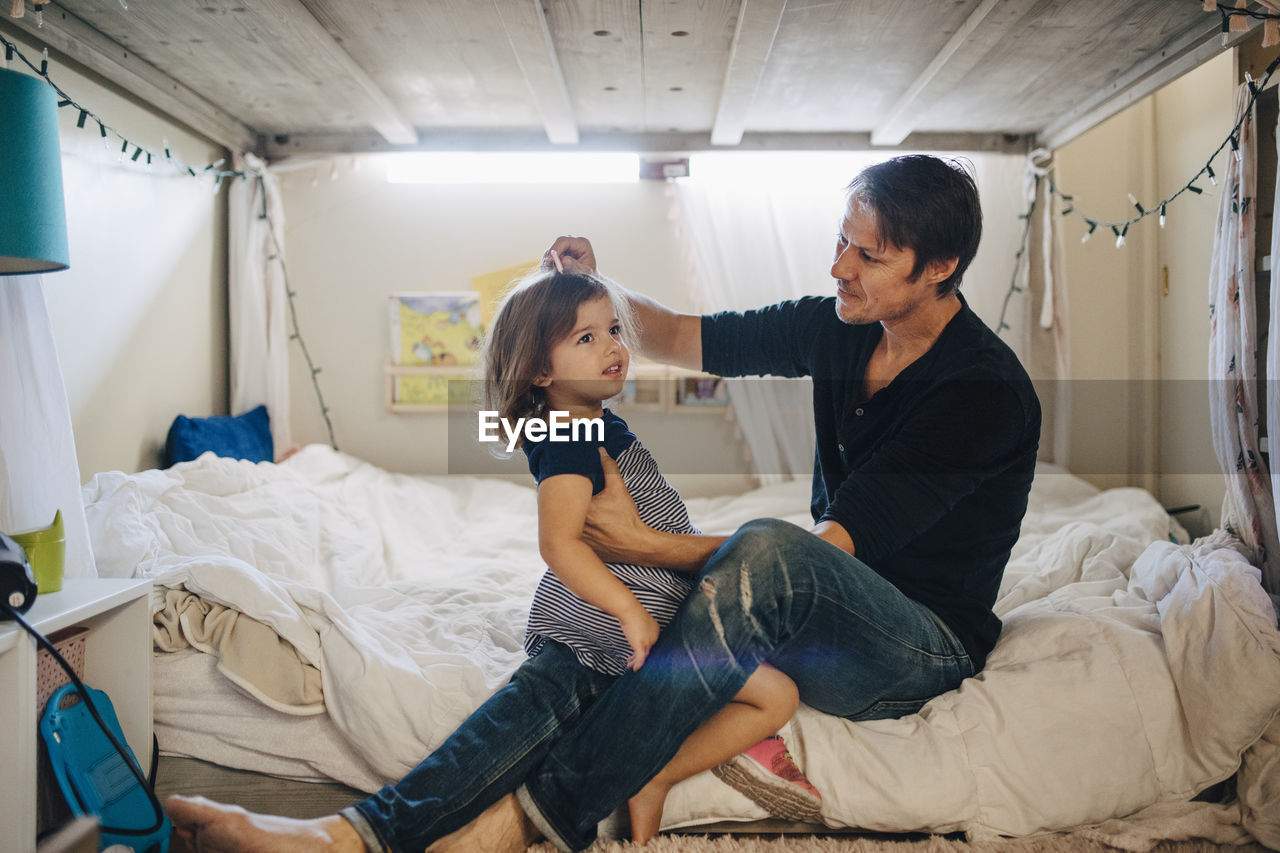 Father combing daughter's hair in bedroom