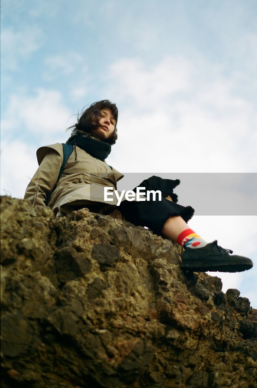 Low angle view of woman sitting on rock against sky