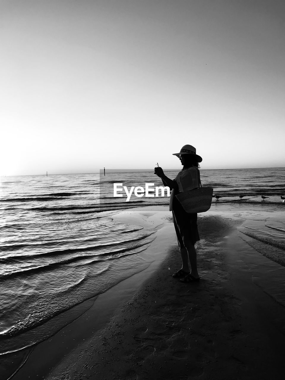 Silhouette woman with bag standing on beach against sky