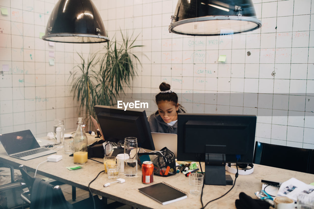 Confident young female programmer coding on laptop at desk in creative office