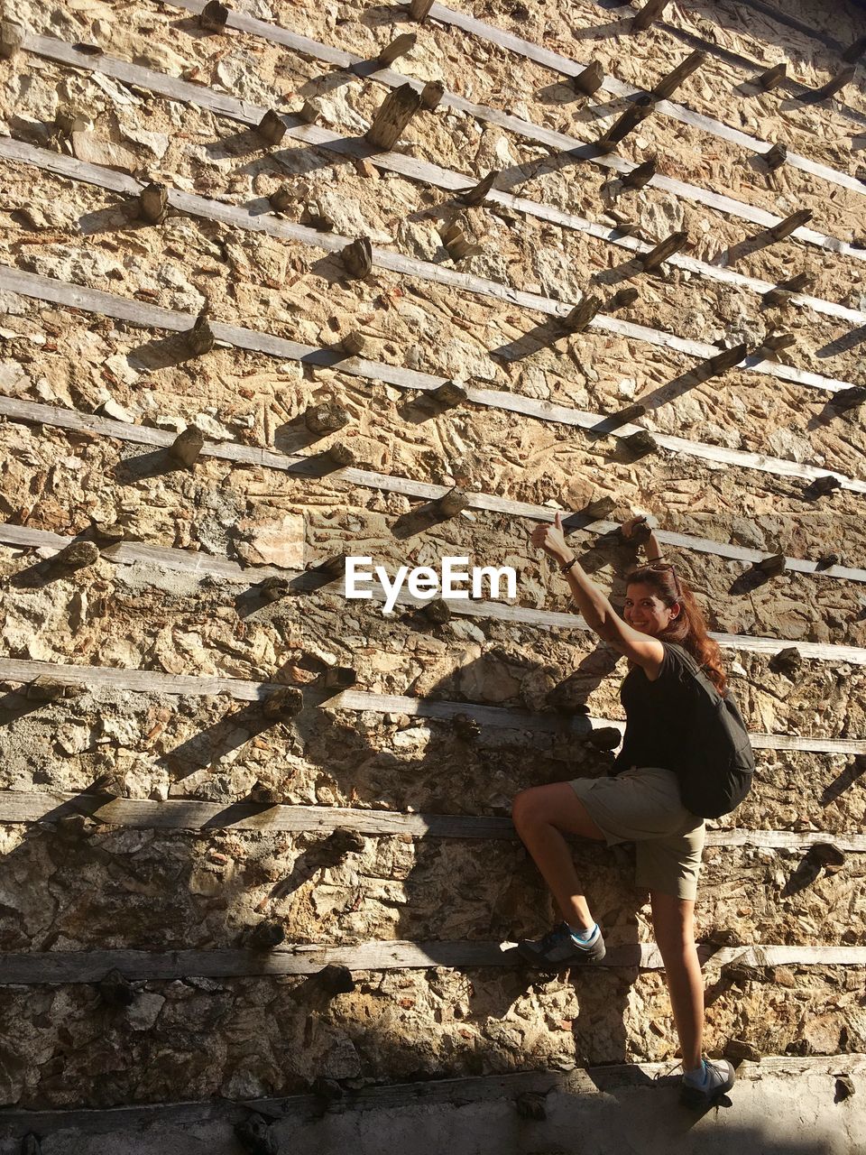 Full length of woman gesturing while climbing on wall